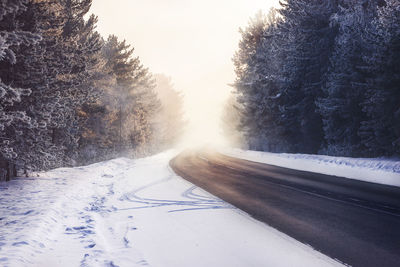 Snow covered road by trees against sky