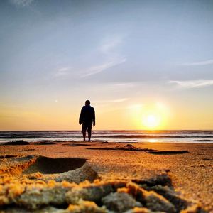Rear view of silhouette man standing on beach during sunset