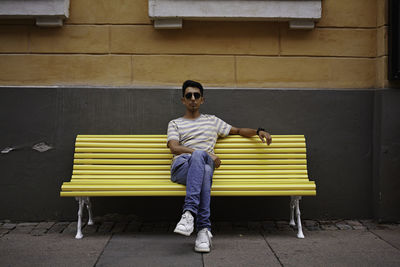 Portrait of man sitting on bench against wall