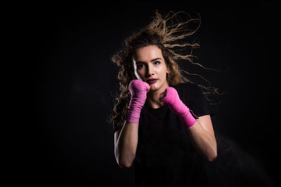 Portrait of female boxer standing against black background