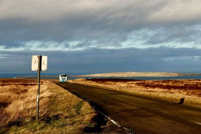 Road sign on field against sky