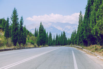Road amidst trees and mountains against sky