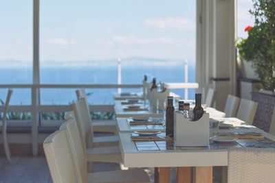Chairs and tables in restaurant by sea against sky