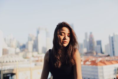 Young woman with long hair sitting against modern buildings in city