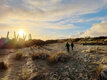 People standing on beach against sky during sunset