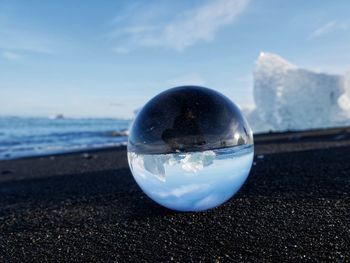 Close-up of crystal ball on beach against sky