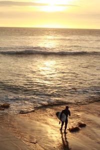 Silhouette of person walking on beach at sunset