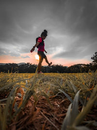 Side view of woman standing on field against sky during sunset