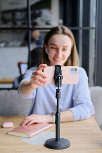 Young beautiful woman blogger making a video for her blog using phone camera in a cafe.