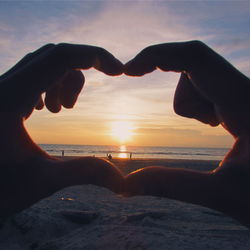 Hands in heart shape on beach at sunset