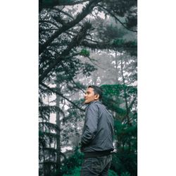 Side view of young man standing against plants