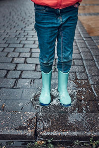 Close up of legs of little girl jumping in puddle wearing rubber boots walking in on rainy day
