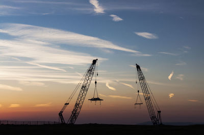 Silhouette cranes at construction site against sky during sunset