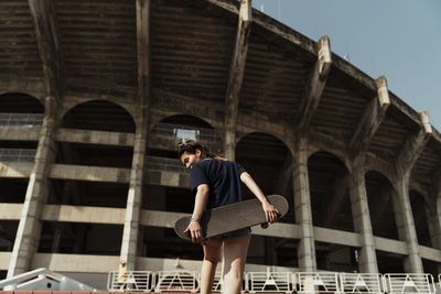 Rear view of woman with skateboard standing against building