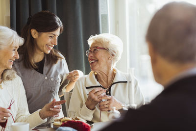 Smiling female healthcare worker talking with senior women knitting in nursing home
