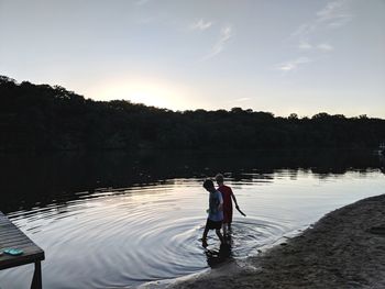 Rear view of man on lake against sky during sunset