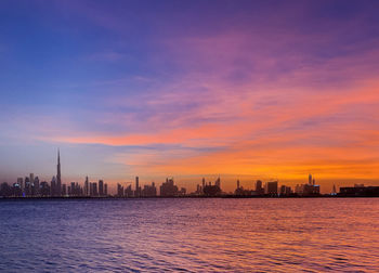 Sea and buildings against sky during sunset