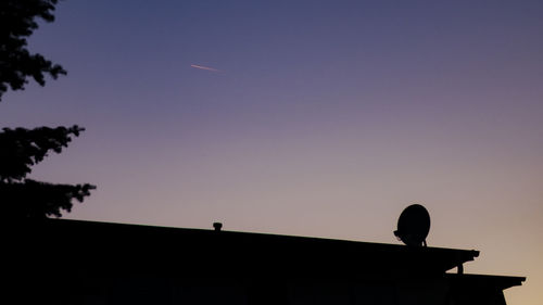 Low angle view of silhouette birds on roof against sky