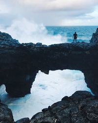 Silhouette man standing on rock by sea against sky