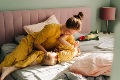 Mom tickles and hugs her little daughter in the morning on the bed in the apartment.