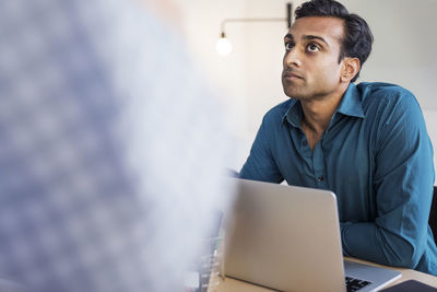 Thoughtful businessman sitting with laptop computer at desk in office