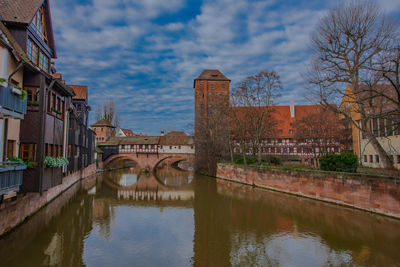 Bridge over river by buildings in city against sky