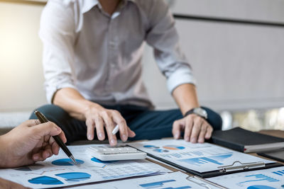 Midsection of businessman discussing charts with colleague on table in office