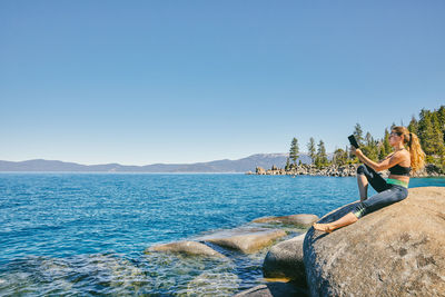 Young woman sitting by lake tahoe reading a kindle book during the day