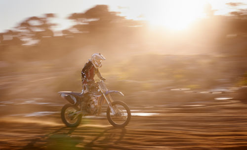 Rear view of man riding bicycle on road against sky during sunset