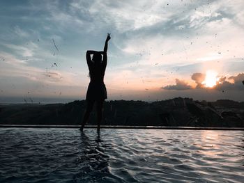 Silhouette woman standing by infinity pool against sky during sunset