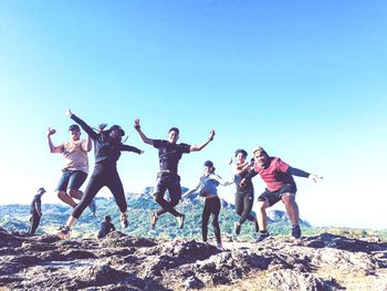 Low angle view of cheerful friends jumping on mountain against clear sky