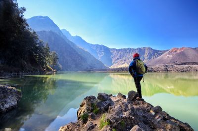 Man standing on rock by lake against sky