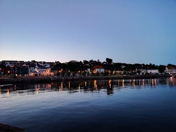 River by illuminated buildings against clear sky at dusk