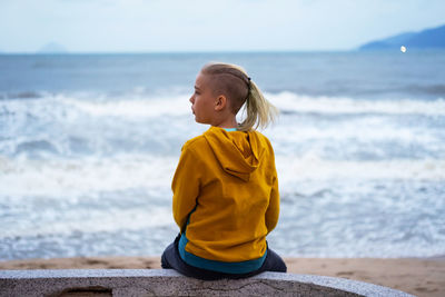 Lonely teenager looking to sea sitting on the waterfront. rear view of teenager against seascape.