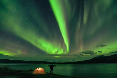 Rear view of man at lakeshore against aurora polaris