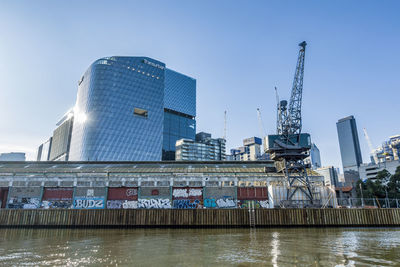 Modern buildings by river against sky in city