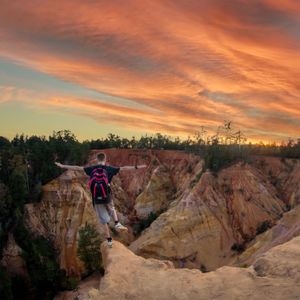 Man standing on rock against sky during sunset