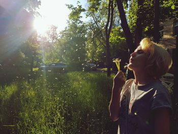 Woman blowing flowers while standing against trees