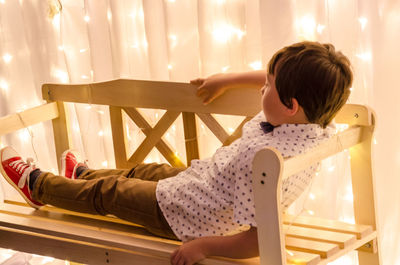 Full length of boy lying down on bench by decorative curtain