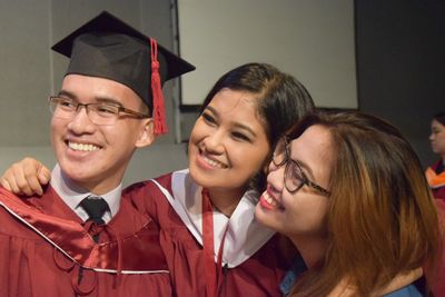 Happy friends wearing graduation gown looking away at university