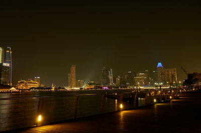 Illuminated buildings by river against sky at night