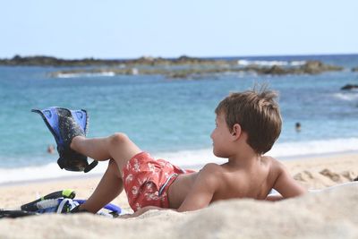 Boy wearing diving flippers and lying on beach