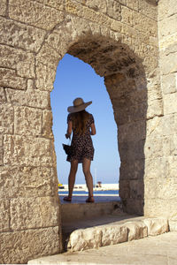 Rear view of woman standing by stone wall against sky