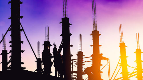 Silhouette cranes at construction site against sky during sunset