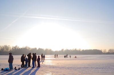 People standing on frozen lake against sky