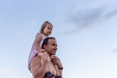 Low angle view of young man and little girl standing against sky