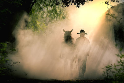 Cowboy walking amidst smoke with horse 