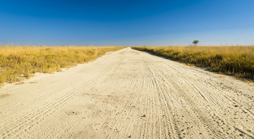 Dirt road amidst land against sky