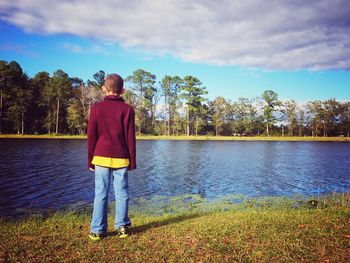 Rear view of man standing by lake against sky