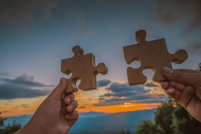 Low section of people holding hands against sky during sunset